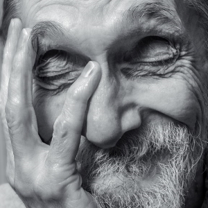 A black&white closeup face self-portrait of a caucasian male, eyes closed, chin resting in left hand palm. The expression is whimsical self-reflection.
