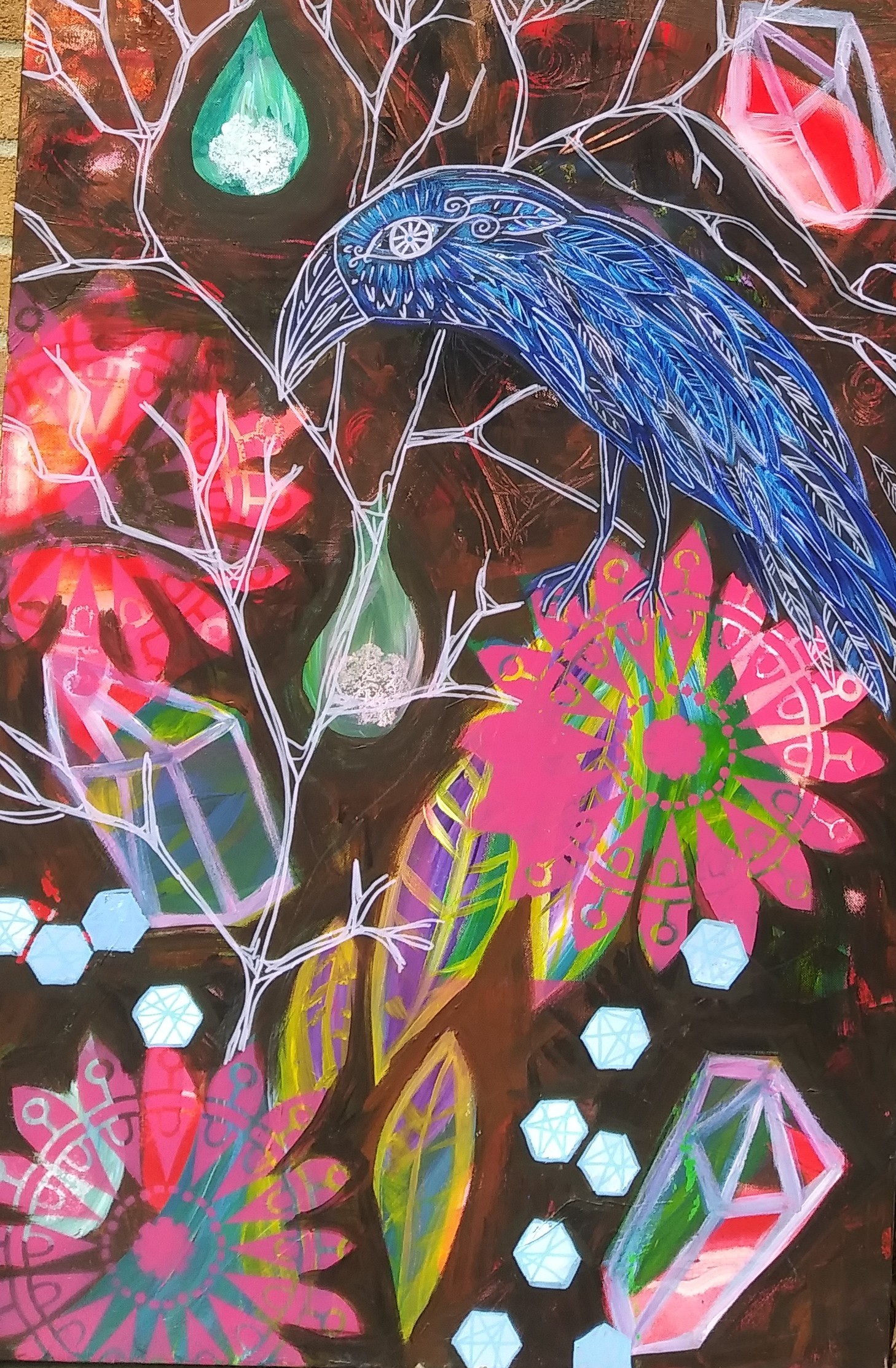 In this painting the background is dark like burnt umber, very deep brown. Floating on top are abstracted images of crystals in bright colors like pink and green outlined in light purple. There are white tree branches drawn in thin lines where a crow sits. The crow is dark blue with white details outlining his feathers and features. Scattered throughout the painting are flowers in bright pink with the pattern of a mandala making their design. Also floating throughout the painting are leaves that also have abstract colors composing their design