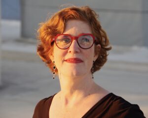 Annie Leist, a white woman with short red hair wearing red framed glasses